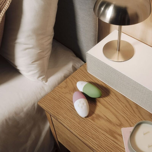 Three colorful stones on a wooden nightstand next to a lamp and cushion.