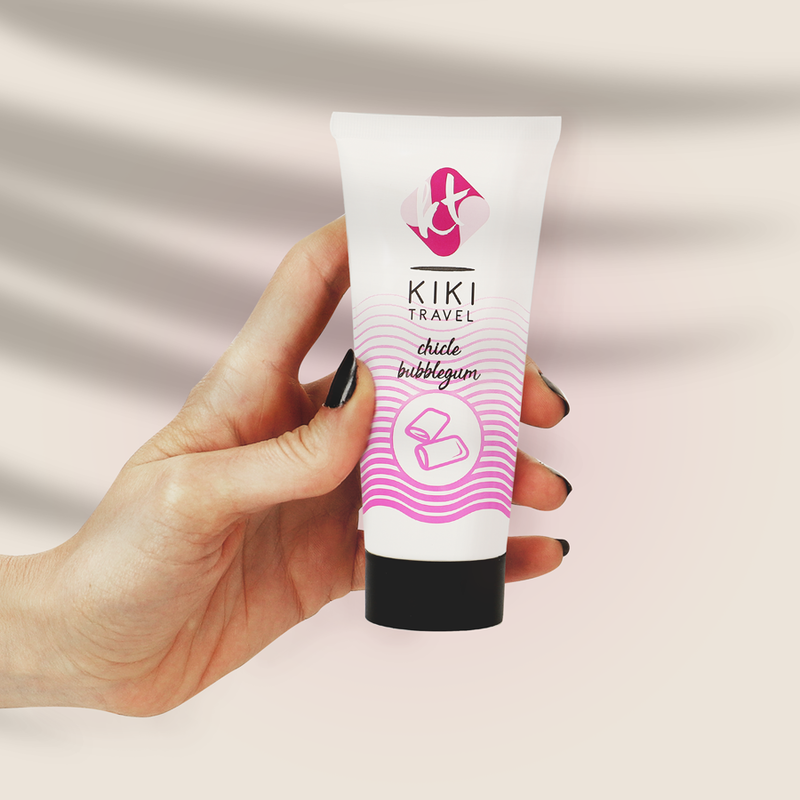 Hand holding a KIKI Travel tube of bubblegum-flavored lip balm against a plain background