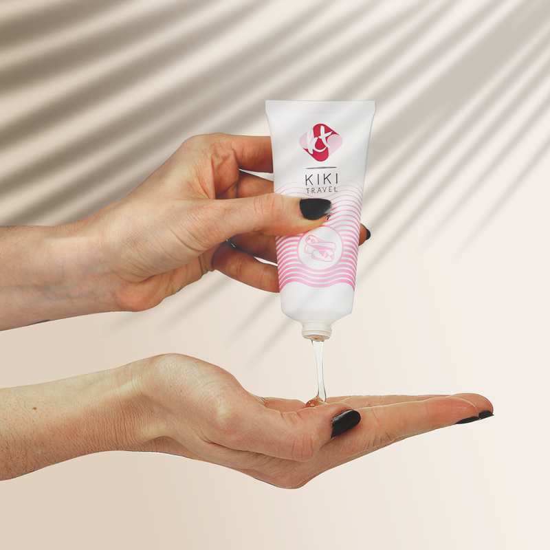 Hand holding a KIKI Travel tube with cream being squeezed onto another hand against a neutral background